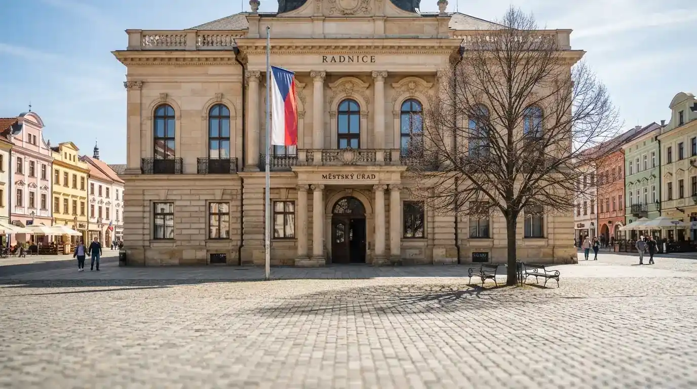 Kamenná budova se sloupy a vlajkou stojí na náměstí za slunečného dne.